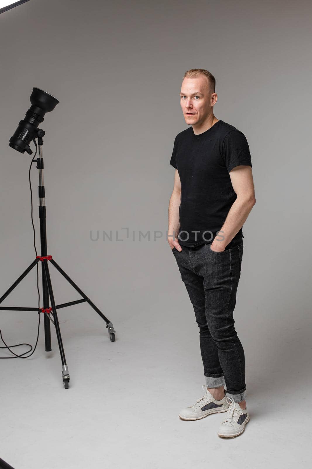 Full-length photo of young Caucasian man in black clothes standing at the studio near