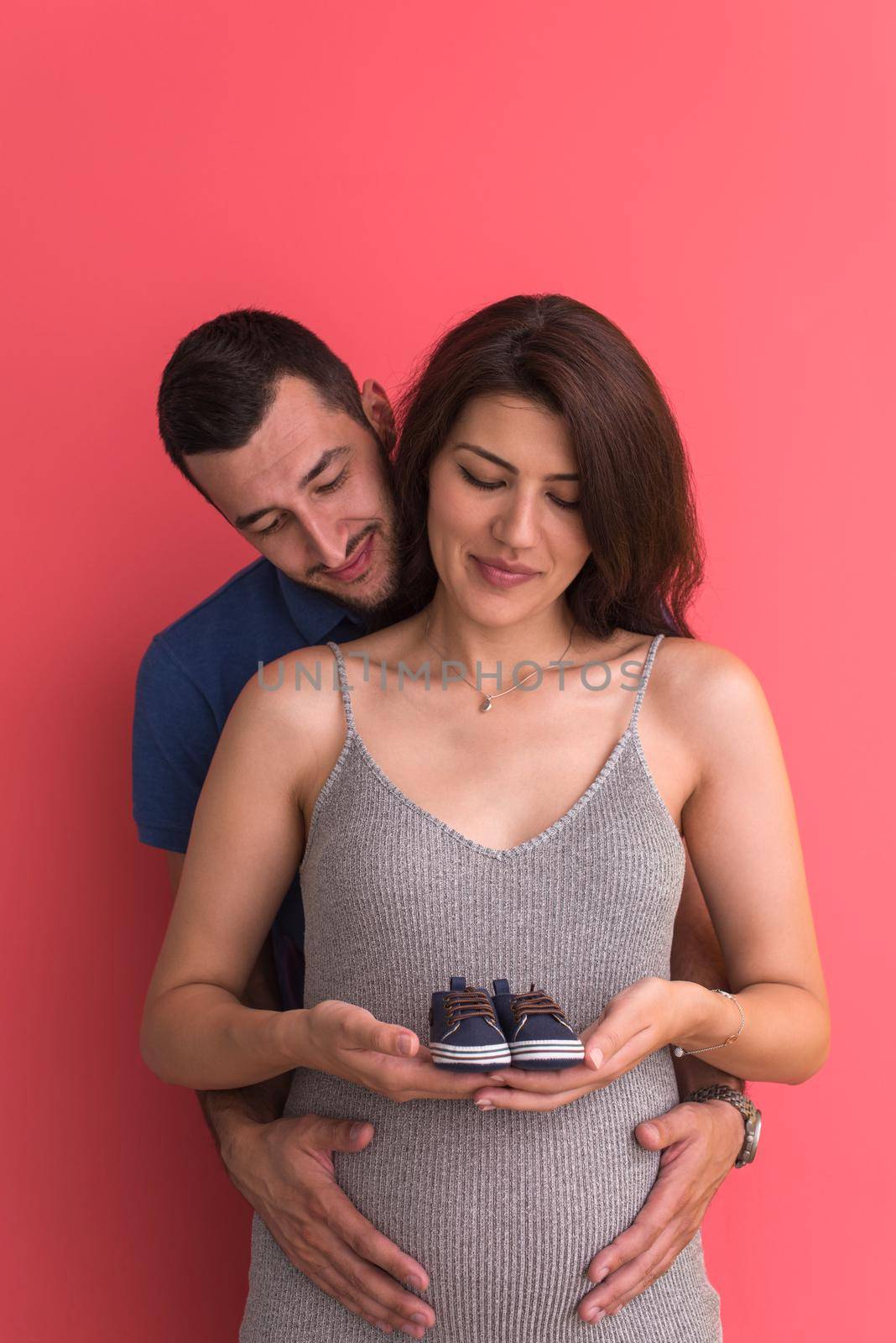 young pregnant couple holding newborn baby shoes by dotshock