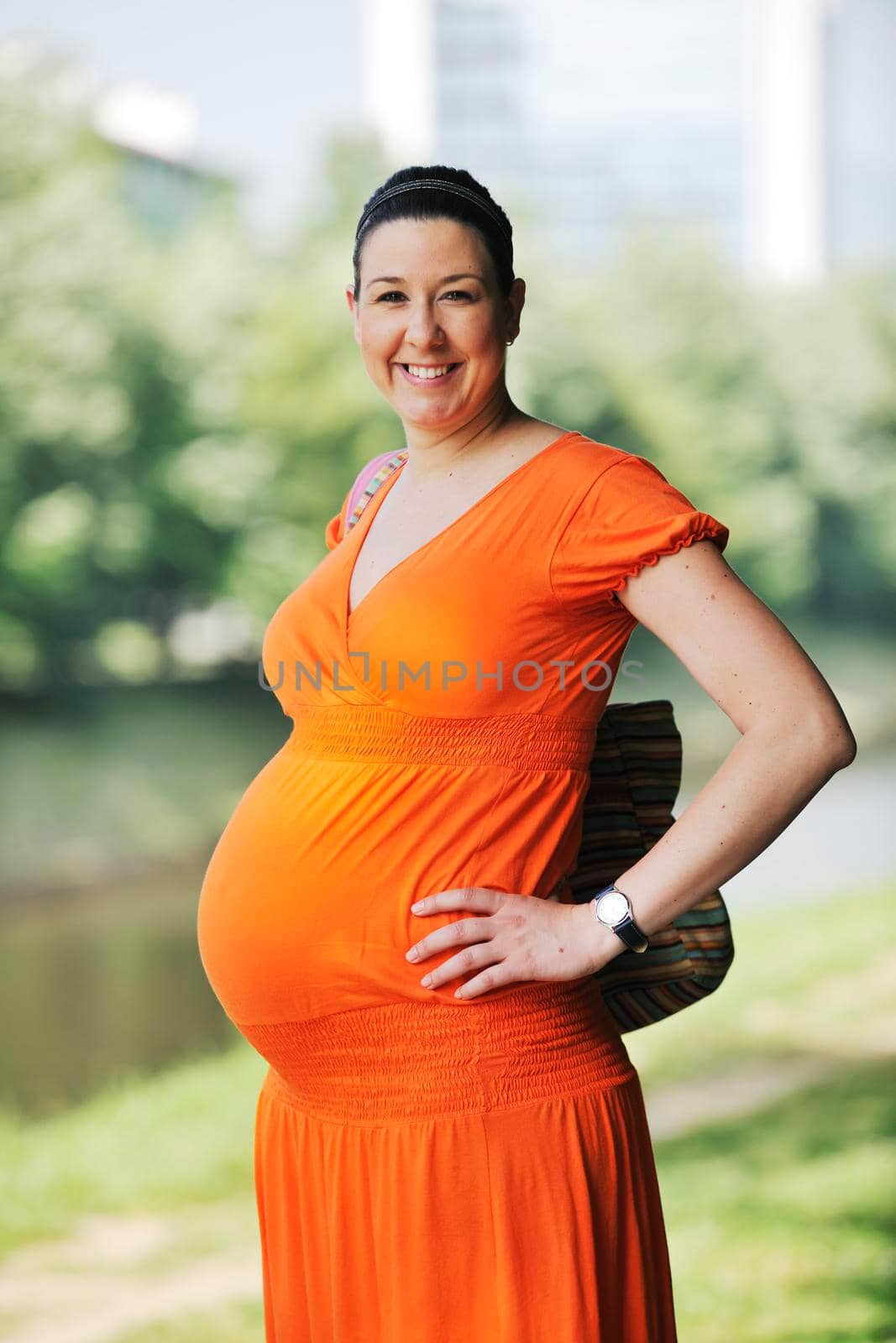 beautiful young happy pregnant woman outdoor in bright nature in orange dress