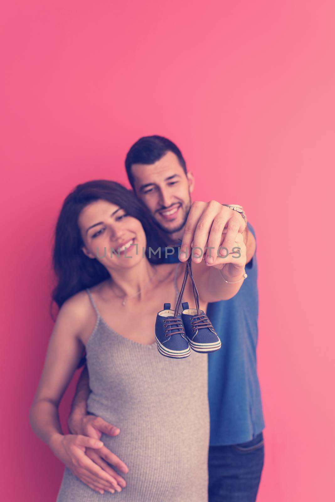 young pregnant couple holding newborn baby shoes by dotshock
