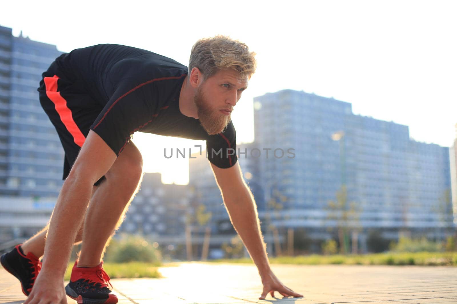 Sporty young man in start position outdoor at sunset or sunrise