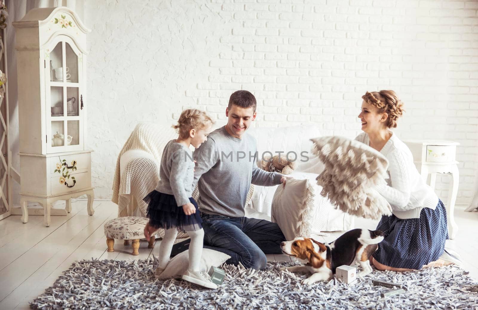 mother,father,five year old daughter and pet dog playing with pillows in the spacious living room on Sunday