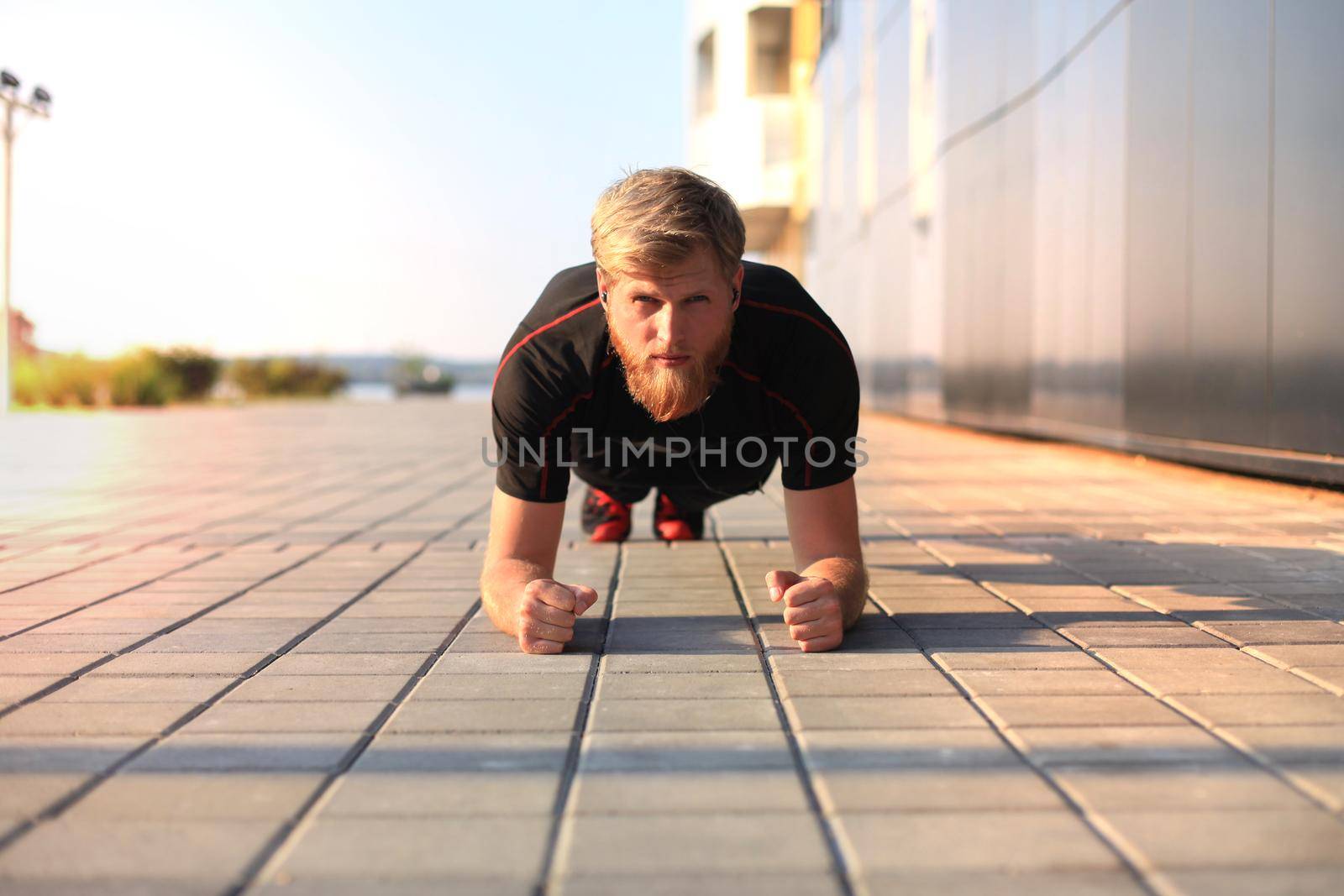 Handsome young man in sports clothing keeping plank position while exercising outdoors