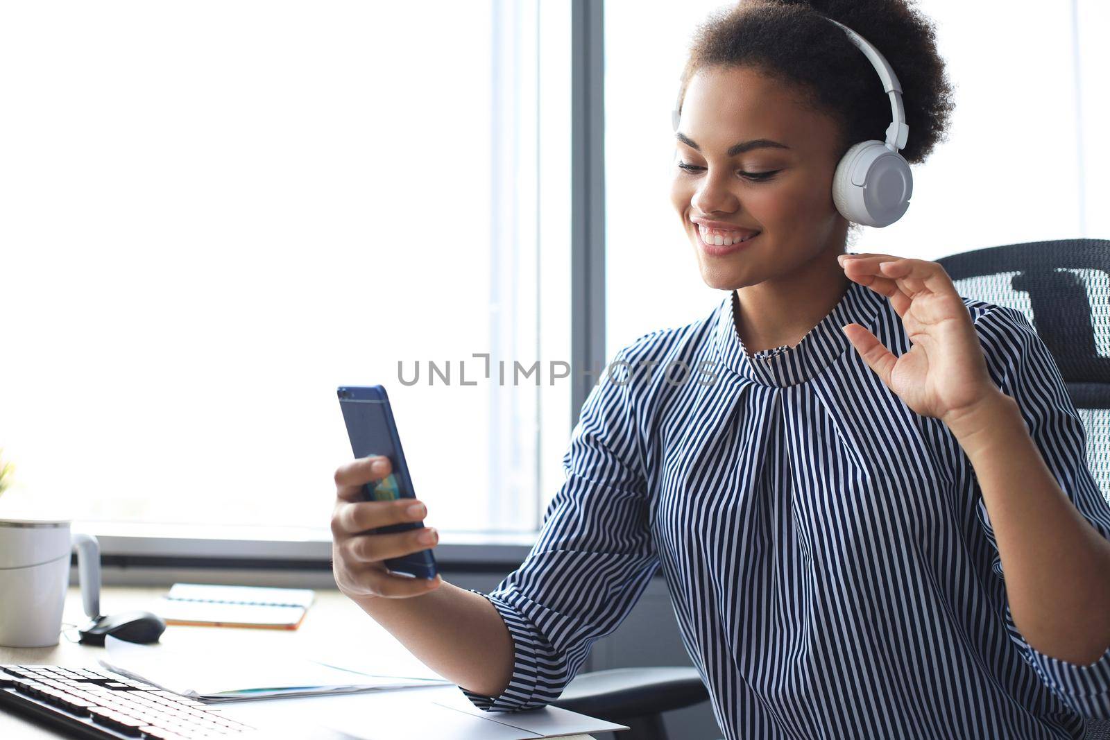 Attractive african american woman doing video call on mobile phone while sitting in earphones