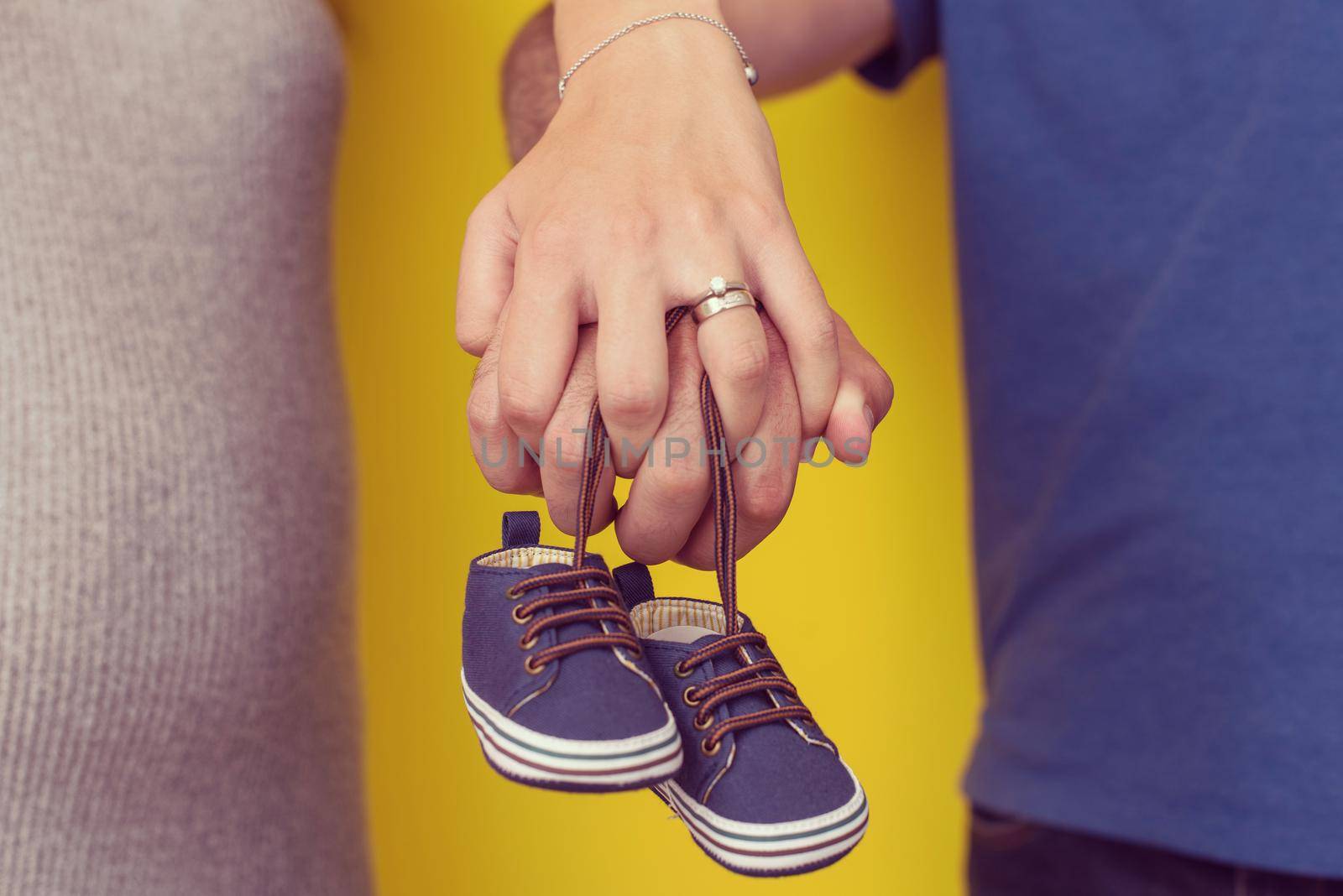 young  pregnant couple holding newborn baby shoes isolated on yellow background,family and parenthood concept