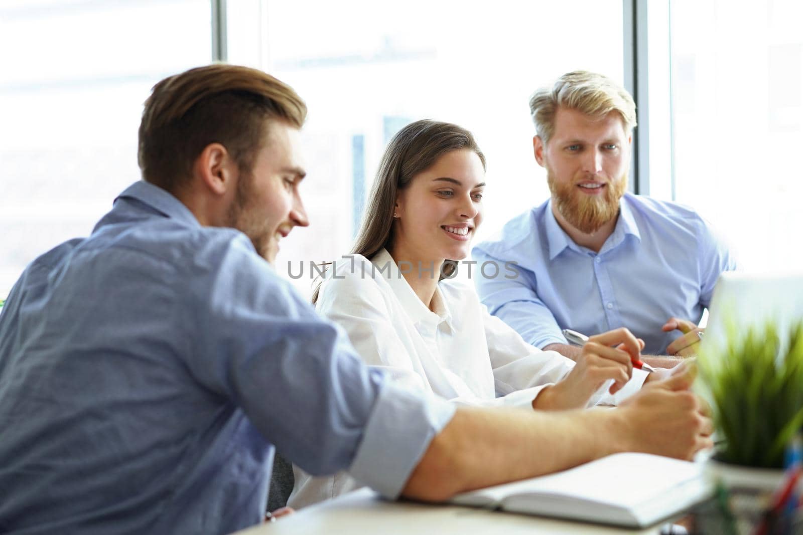 Group of young modern people in smart casual wear pointing at laptop and smiling while sitting in the office. by tsyhun