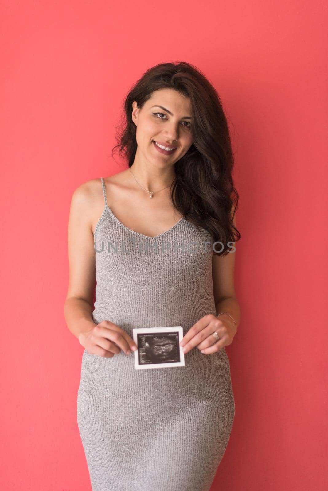 smiling pregnant woman showing ultrasound picture of her unborn baby isolated on red background