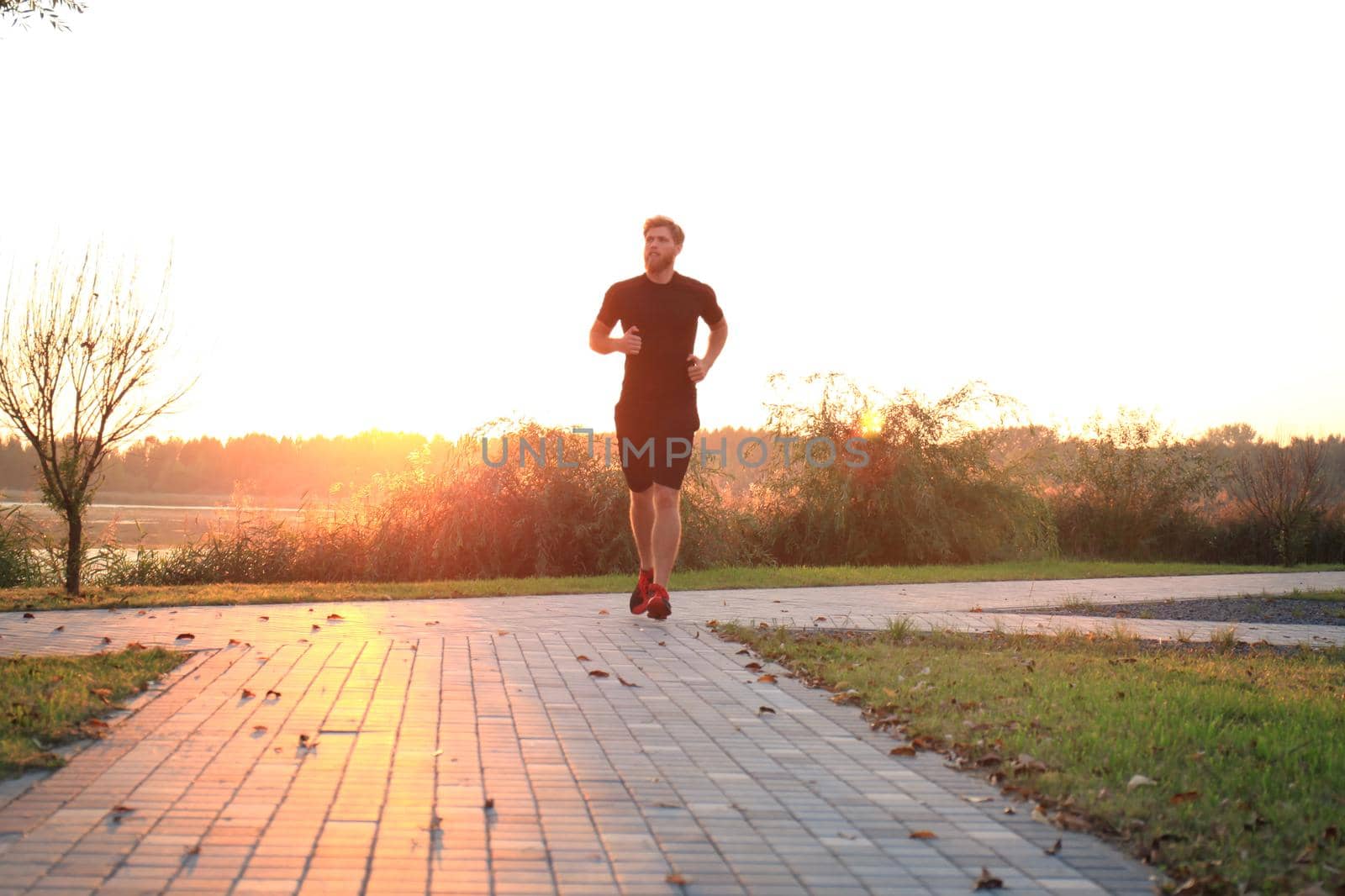 Sporty young man running outdoors to stay healthy, at sunset or sunrise. Runner by tsyhun
