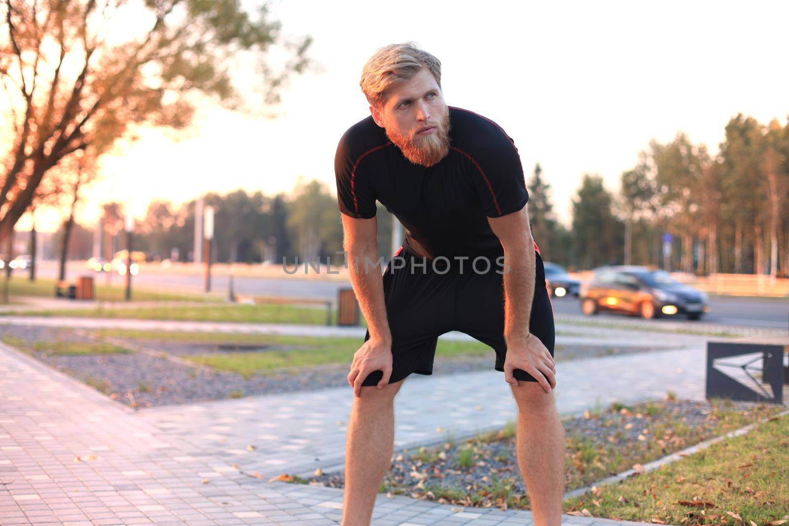 Handsome young man after run resting after jog at the park at sunset or sunrise. by tsyhun