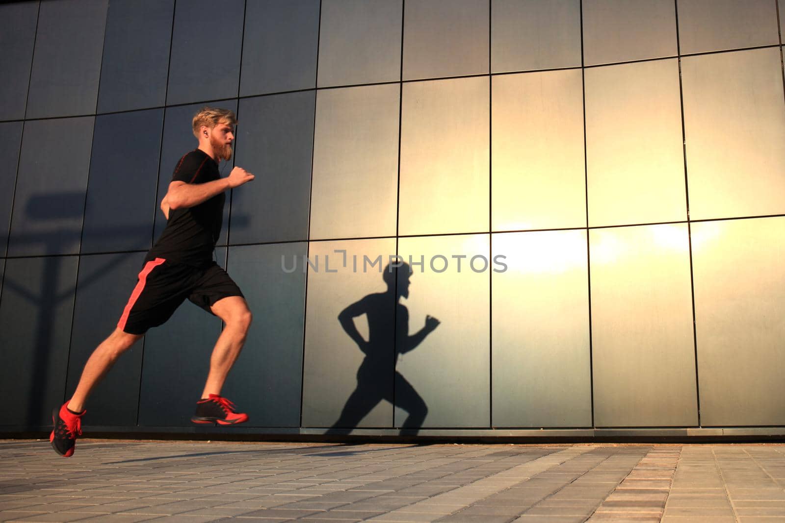 Sporty young man running outdoors to stay healthy, at sunset or sunrise. Runner by tsyhun
