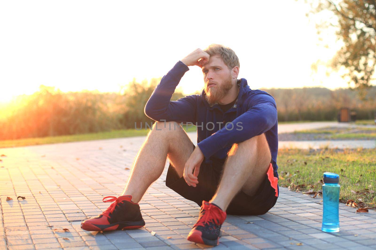 Handsome young man after run resting after jog at the park at sunset or sunrise by tsyhun