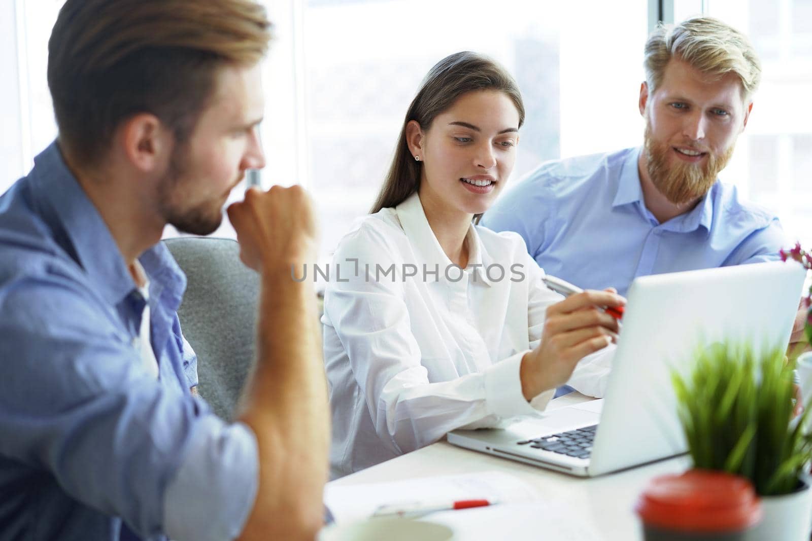 Group of young modern people in smart casual wear pointing at laptop and smiling while sitting in the office.