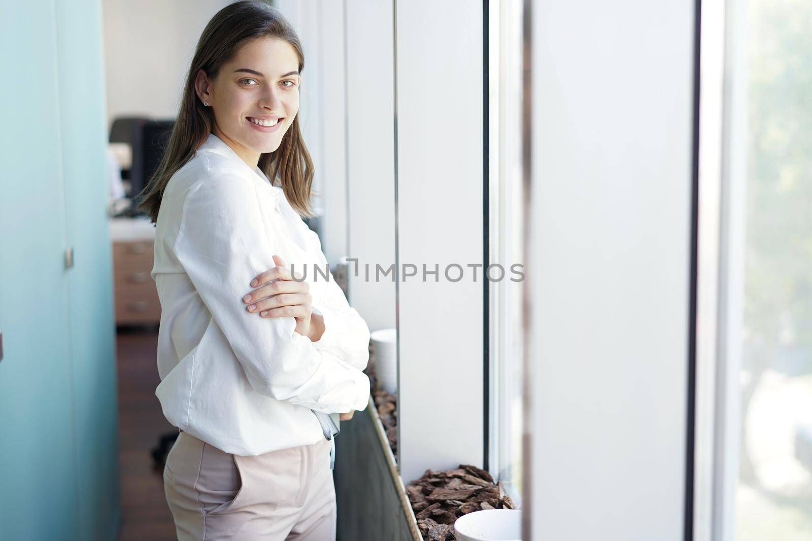 Beautiful business lady is looking at camera and smiling while working in office. by tsyhun