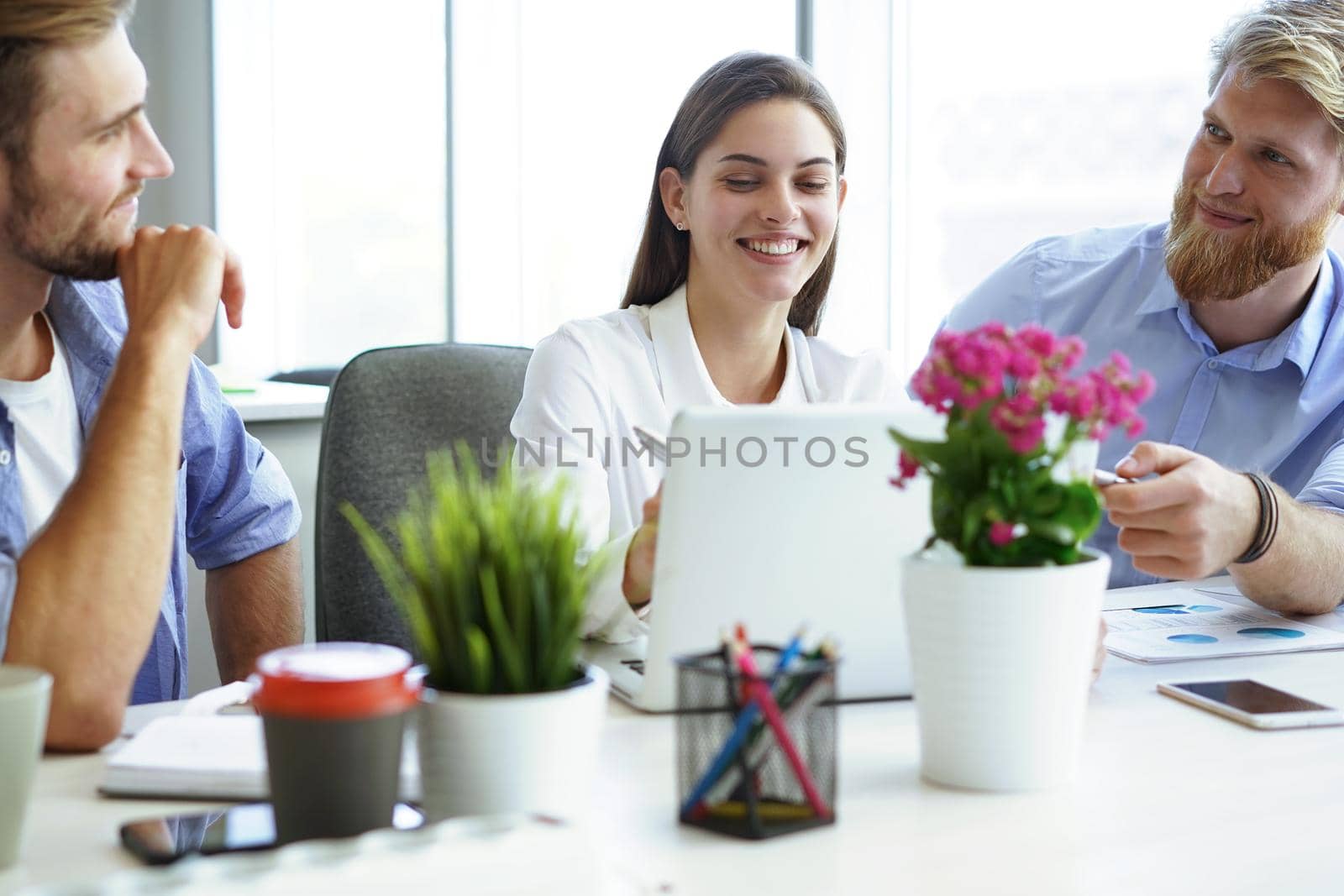 Group of young modern people in smart casual wear pointing at laptop and smiling while sitting in the office. by tsyhun