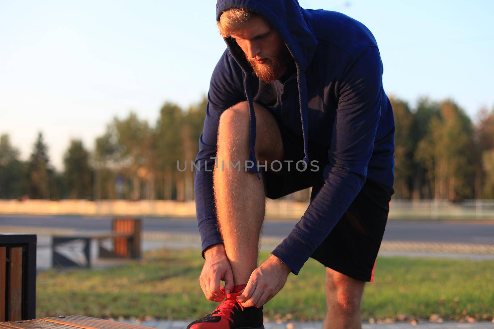 Fit athlete. Handsome adult man runner tying shoelaces at sunset or sunrise. by tsyhun