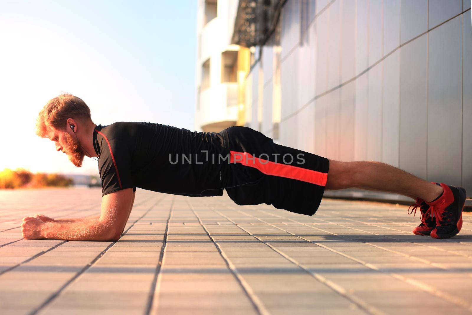 Handsome young man in sports clothing keeping plank position while exercising outdoors