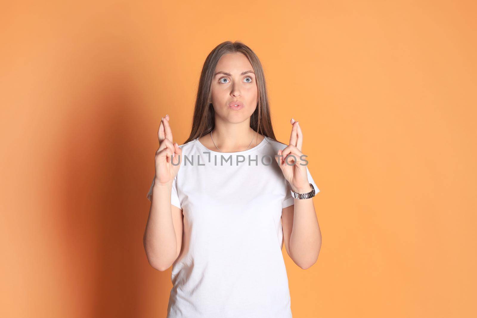 Young woman in basic clothing with fingers crossed isolated over yellow background. by tsyhun