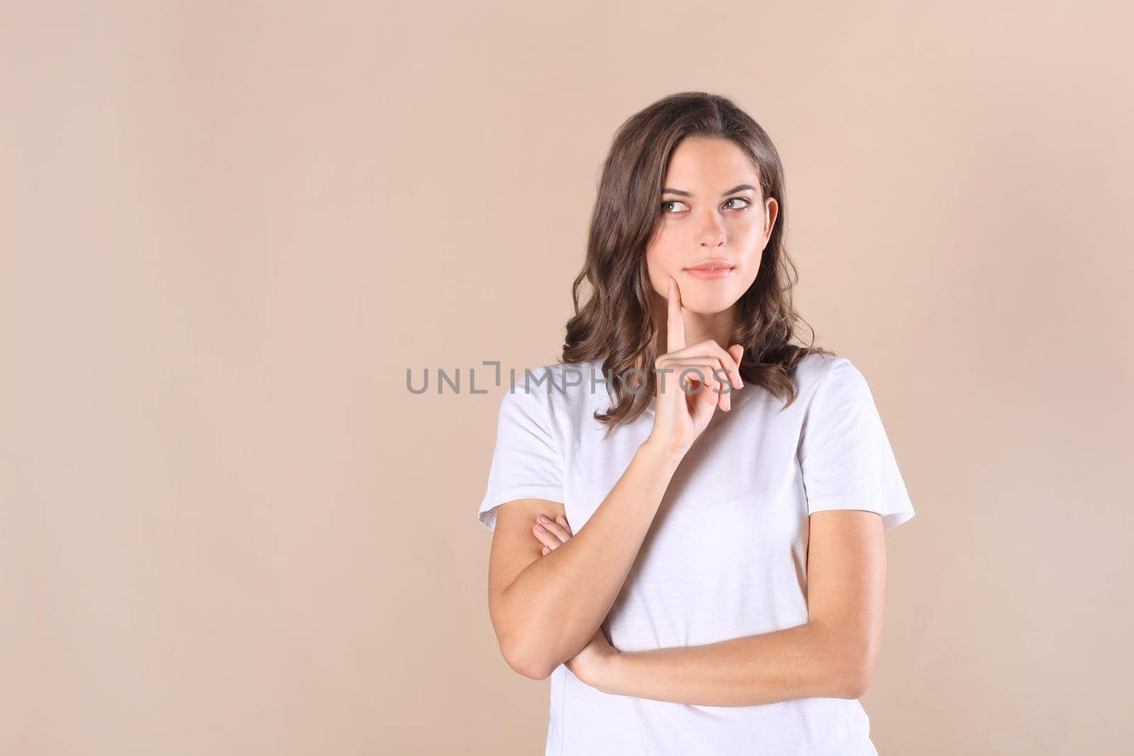 Cheerful brunette woman dressed in basic clothing looking at camera, isolated on beige background by tsyhun