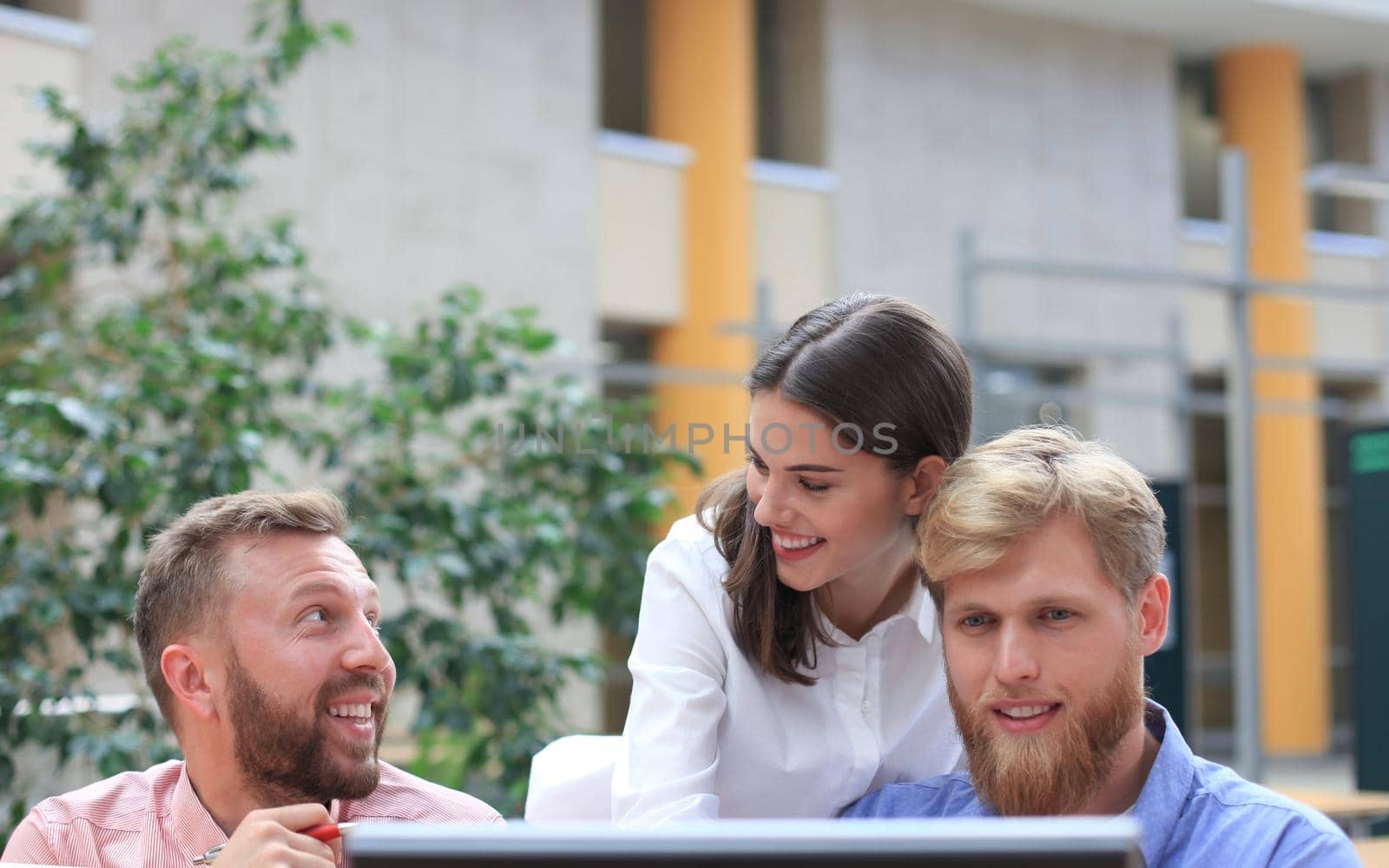 Group of young people in casual wear sitting at the office desk and discussing something while looking at PC together