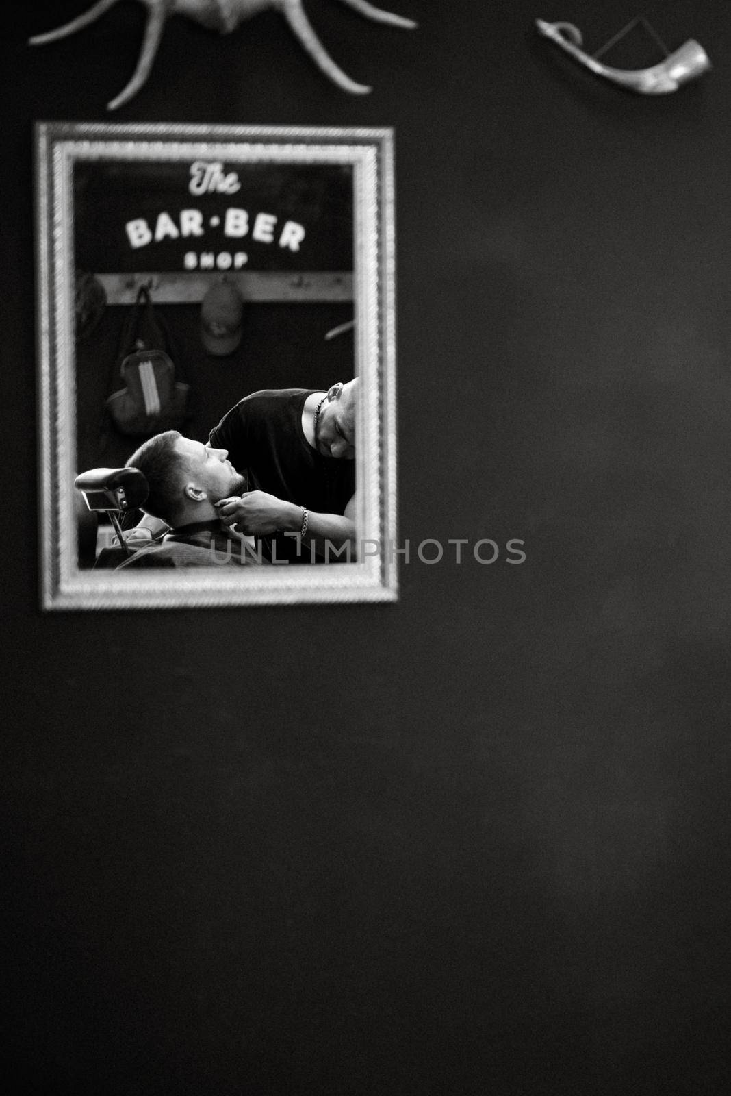 the master in the barbershop shaves and cuts the man in front of the mirror