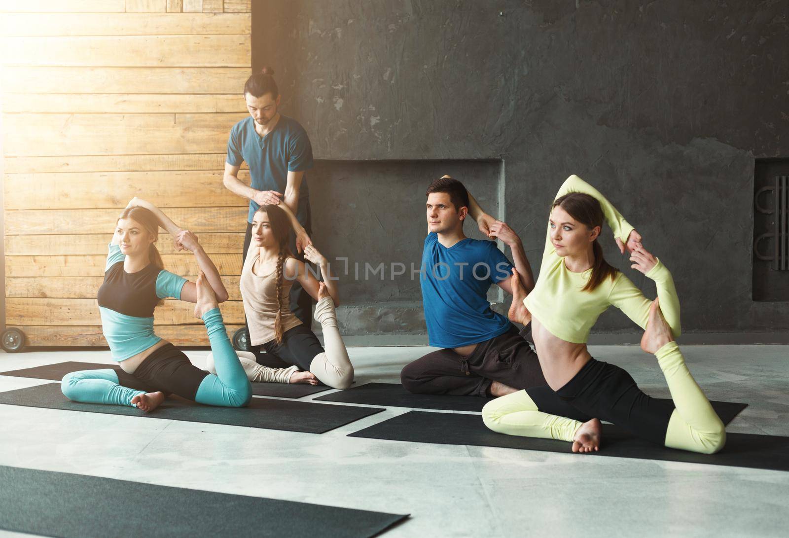 Yoga teacher and beginners in class, making asana exercises. Mermaid pose. Healthy lifestyle in fitness club. Stretching with coach