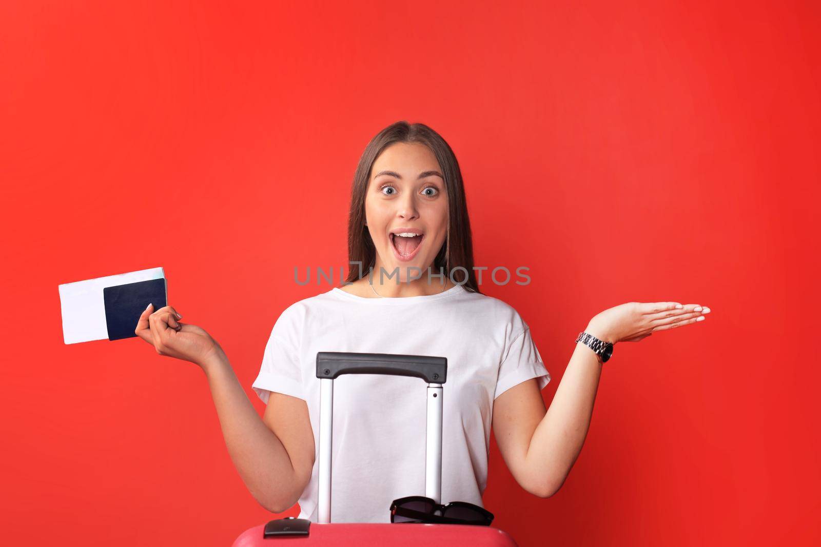 Young tourist girl in summer casual clothes, with sunglasses, red suitcase, passport isolated on red background.