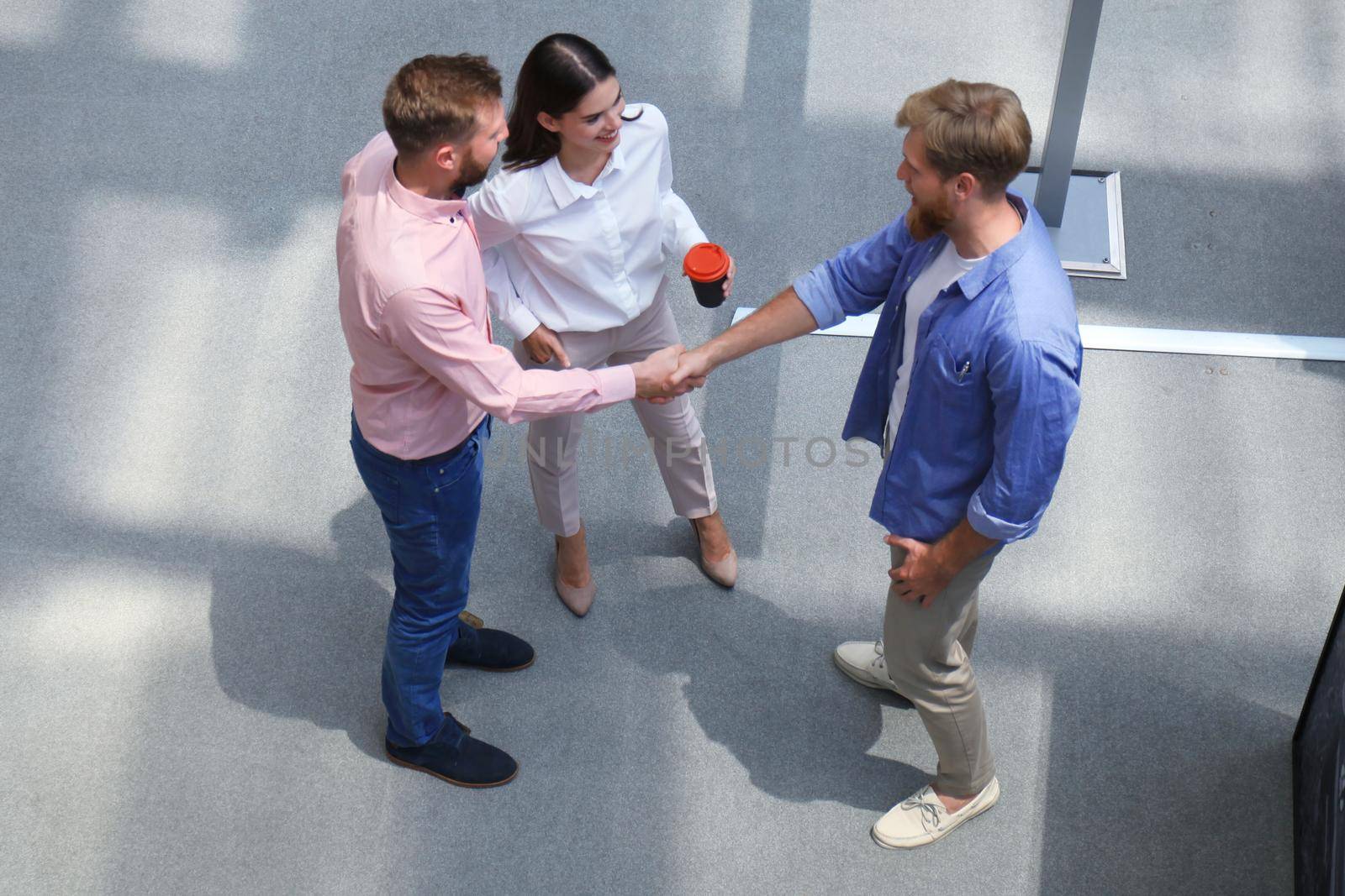 Top view of young modern people in smart casual wear shaking hands standing with their colleagues in creative office