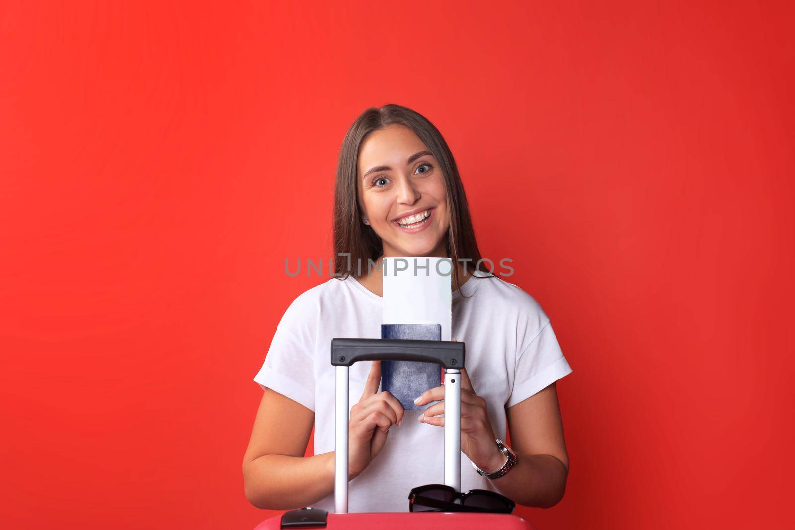 Young tourist girl in summer casual clothes, with sunglasses, red suitcase, passport isolated on red background. by tsyhun