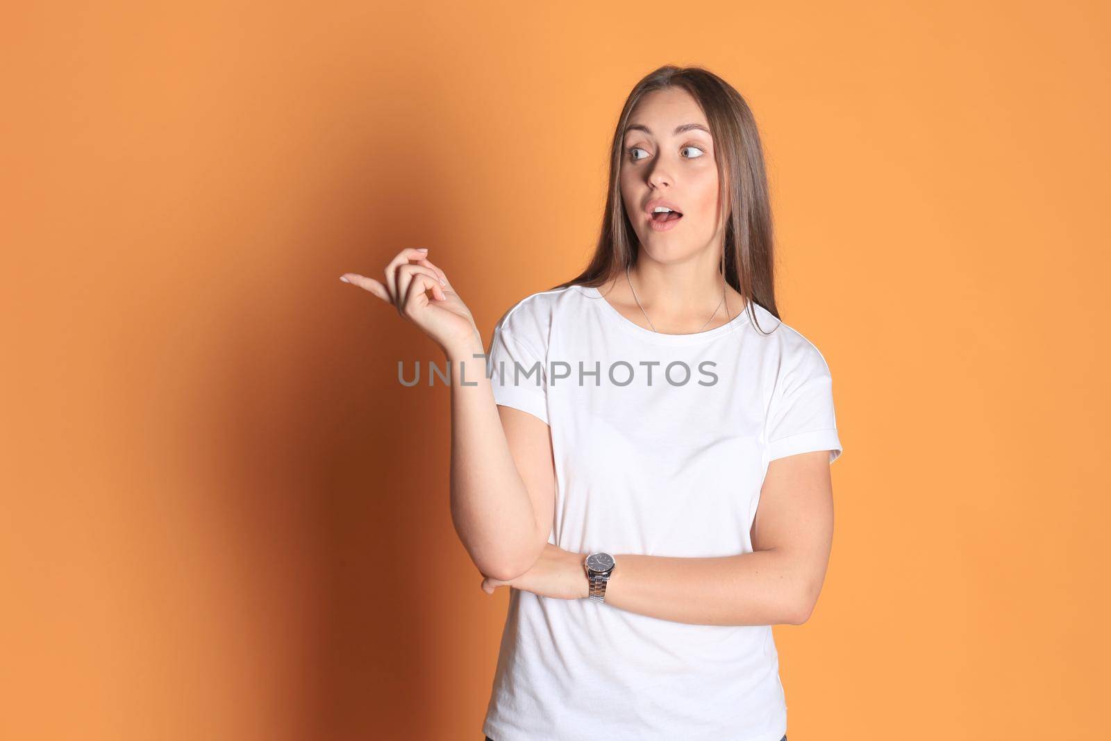 Young woman in basic clothing smiling and pointing finger at copyspace isolated on yellow background. by tsyhun