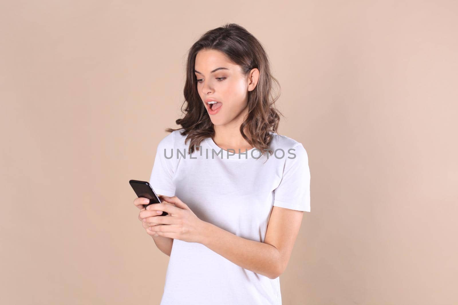 Young woman dressed in basic clothing isolated on beige background, using mobile phone