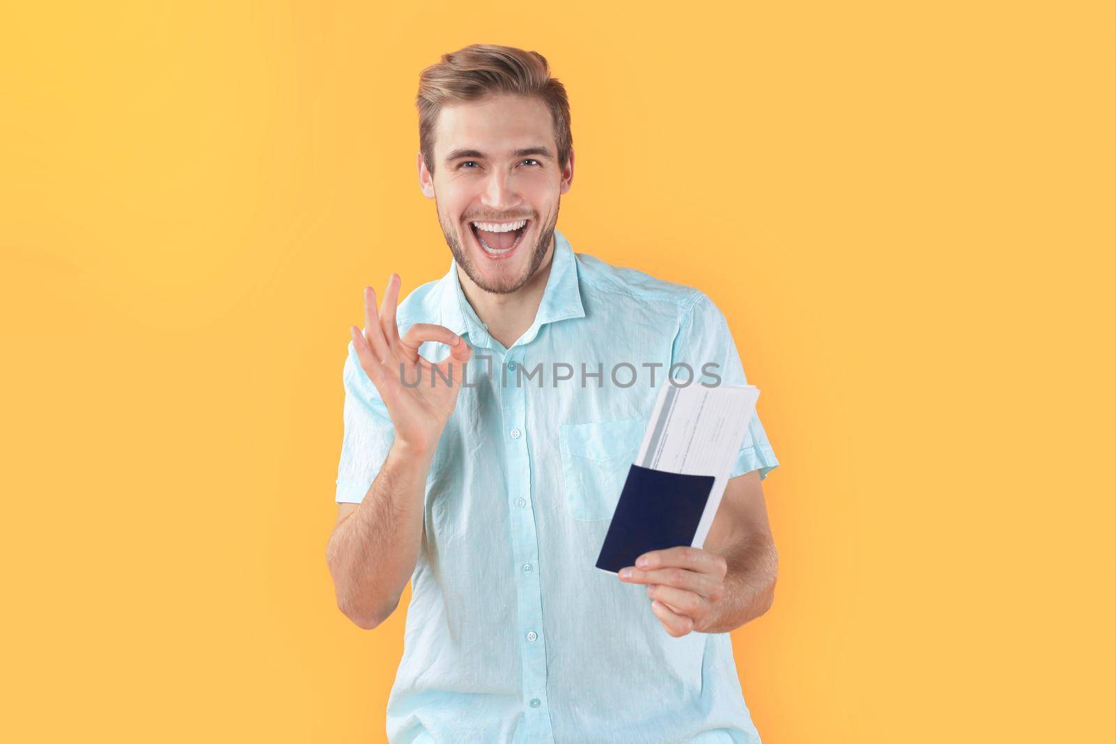 Young man isolated over yellow background holding passport pointing