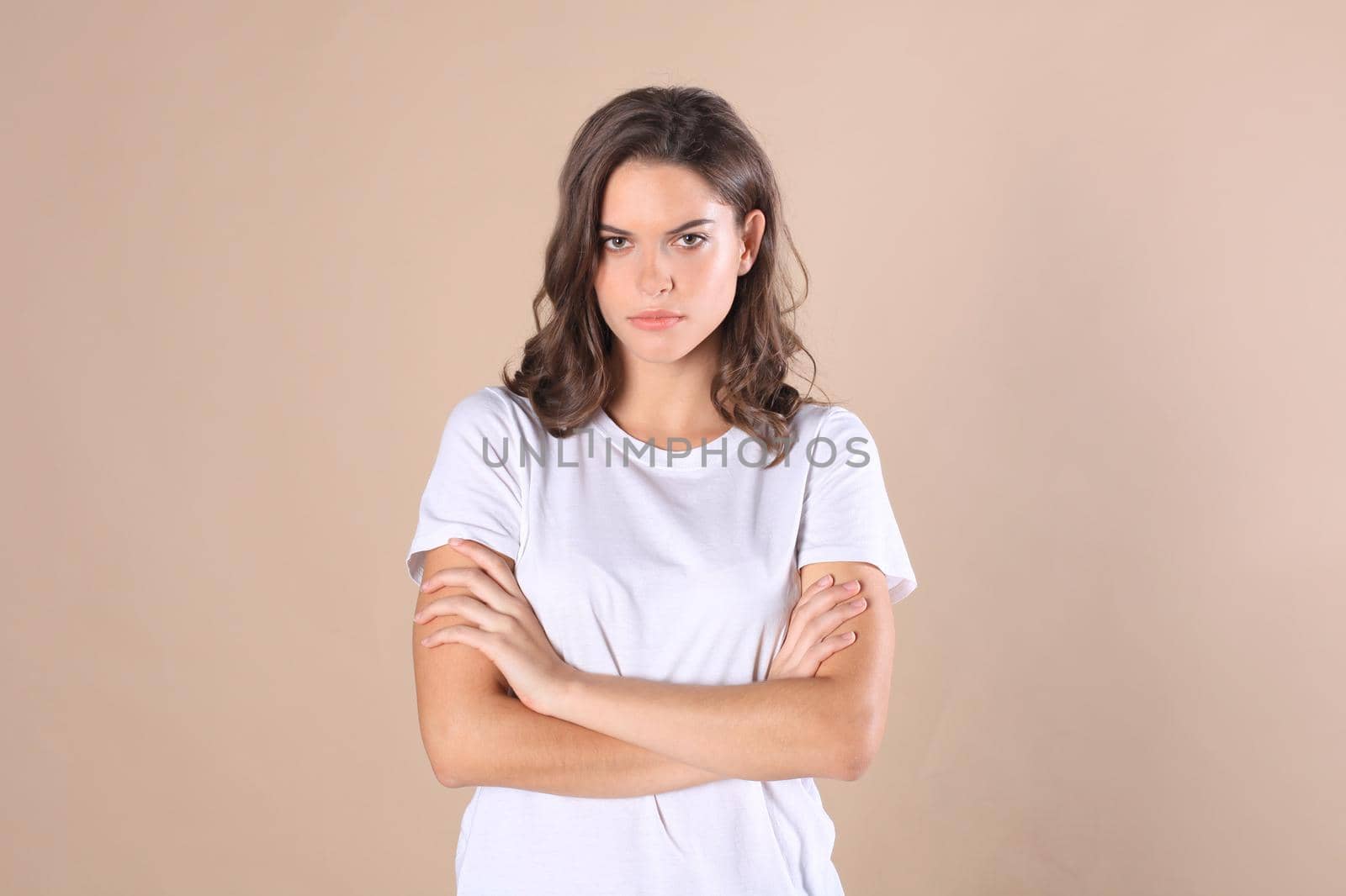 Cheerful brunette woman dressed in basic clothing looking at camera, isolated on beige background by tsyhun