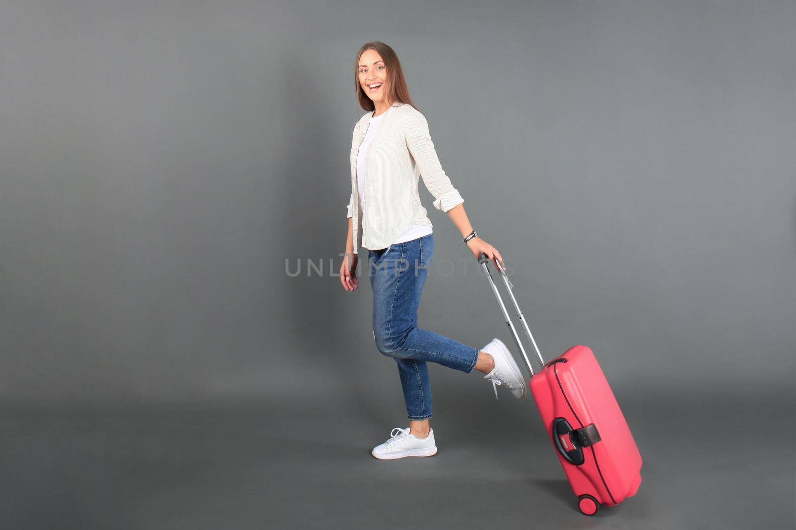 Young tourist girl in summer casual clothes, with sunglasses, red suitcase, passport, tickets isolated grey background.