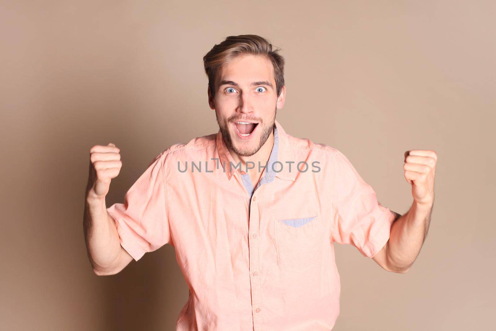 Young man celebrating success standing isolated over beige background