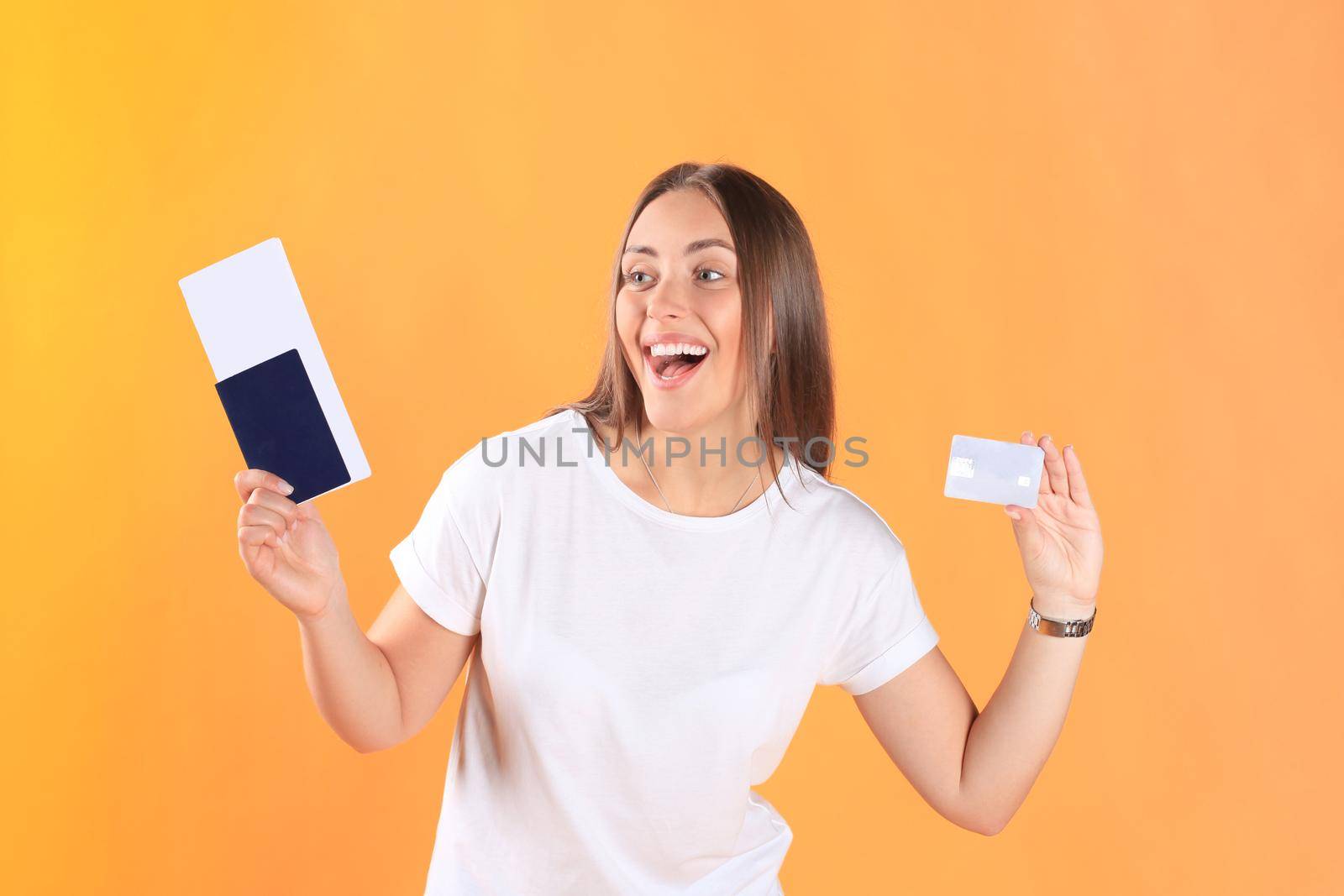 Excited young woman tourist standing isolated on yellow background holding passport with tickets, plastic credit card.