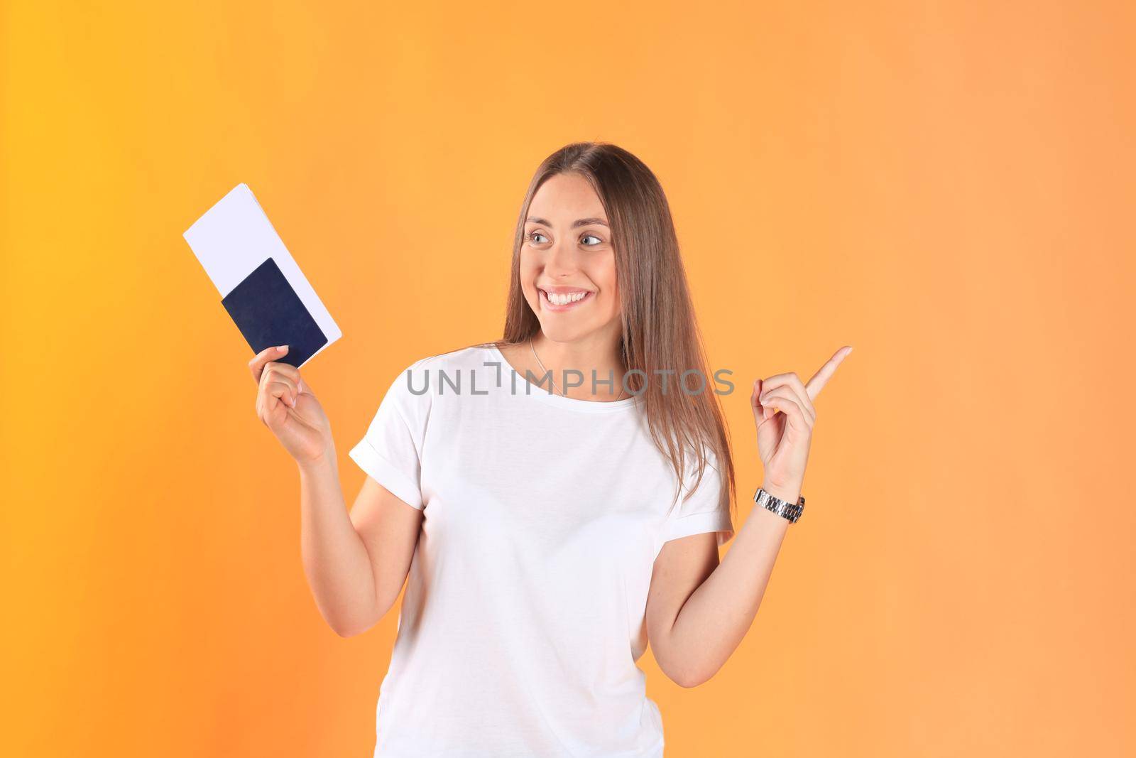 Excited young woman tourist standing isolated on yellow background holding passport with tickets.