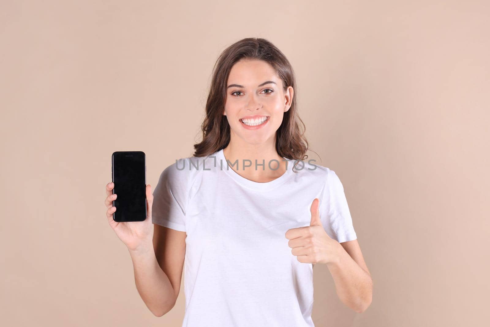Young woman dressed in basic clothing isolated on beige background, using mobile phone