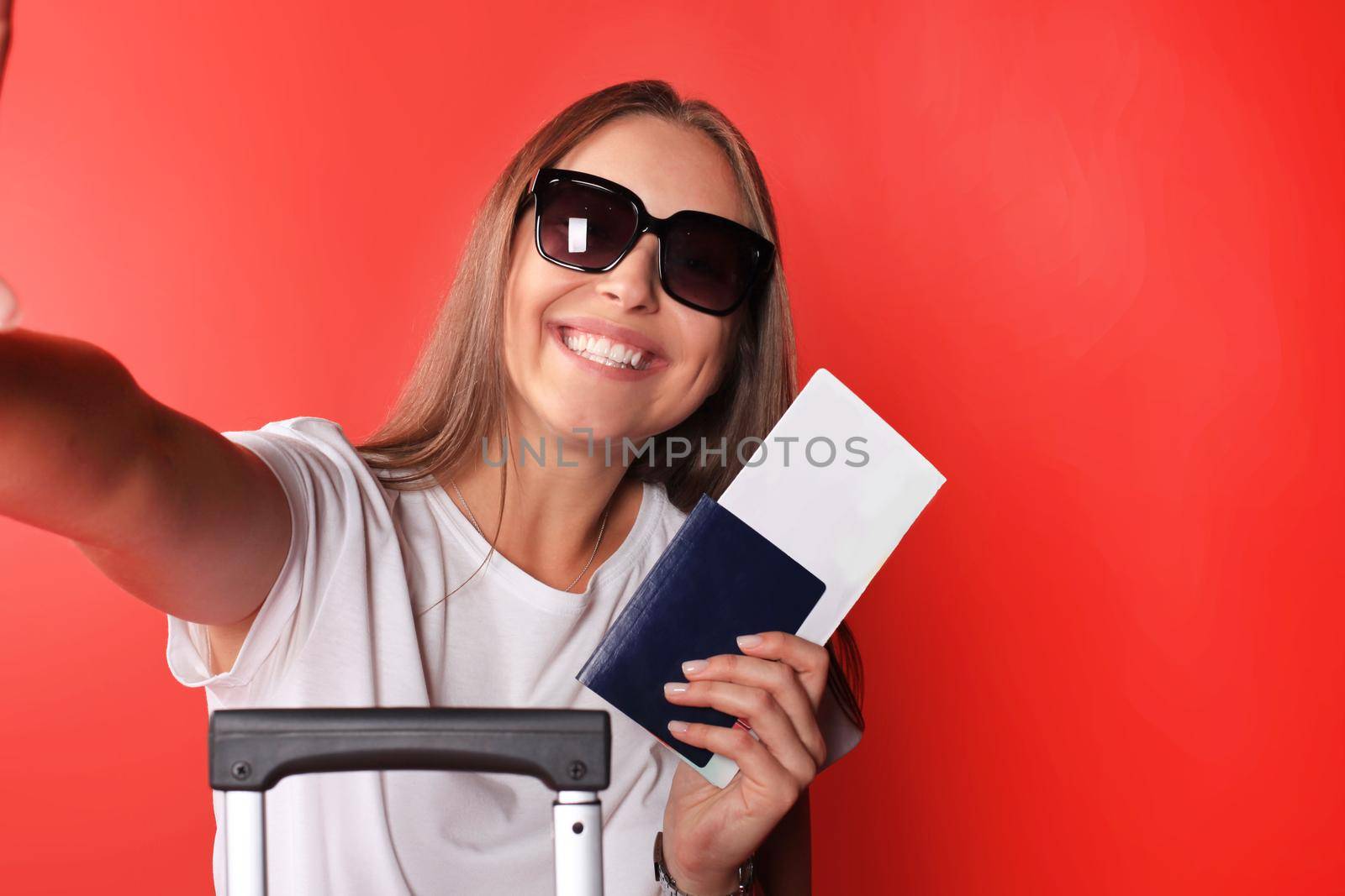 Young tourist girl in summer casual clothes, with sunglasses, red suitcase, passport isolated on red background.