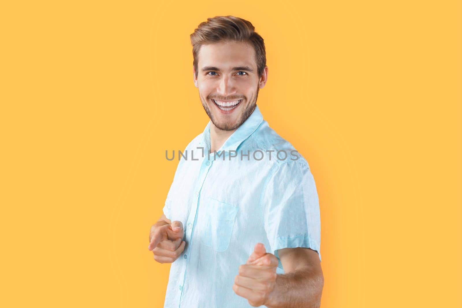 Young man pointing at camera isolated over yellow background