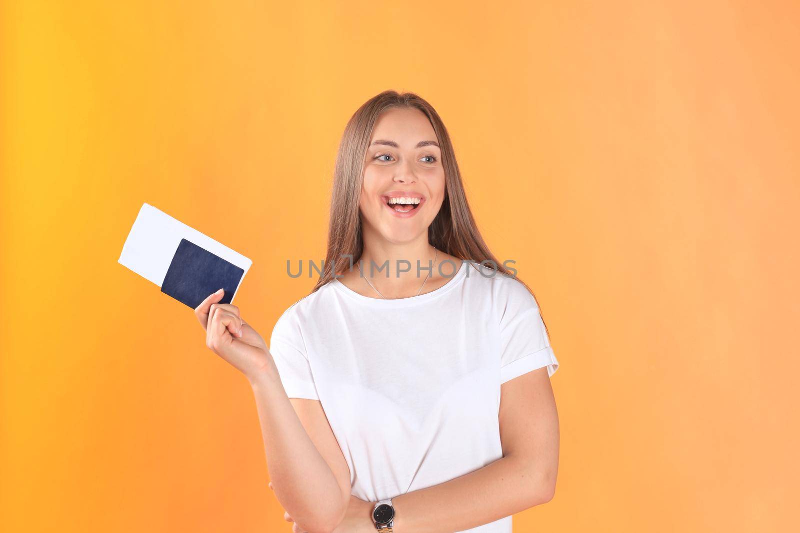 Excited young woman tourist standing isolated on yellow background holding passport with tickets.