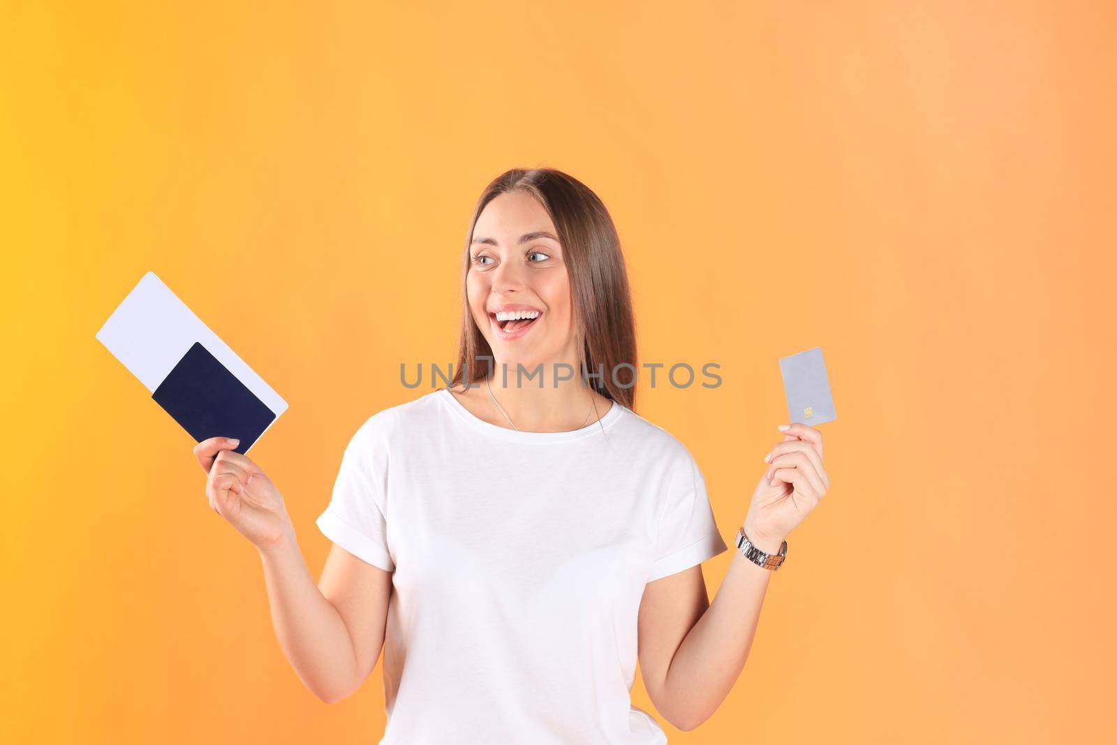 Excited young woman tourist standing isolated on yellow background holding passport with tickets, plastic credit card.