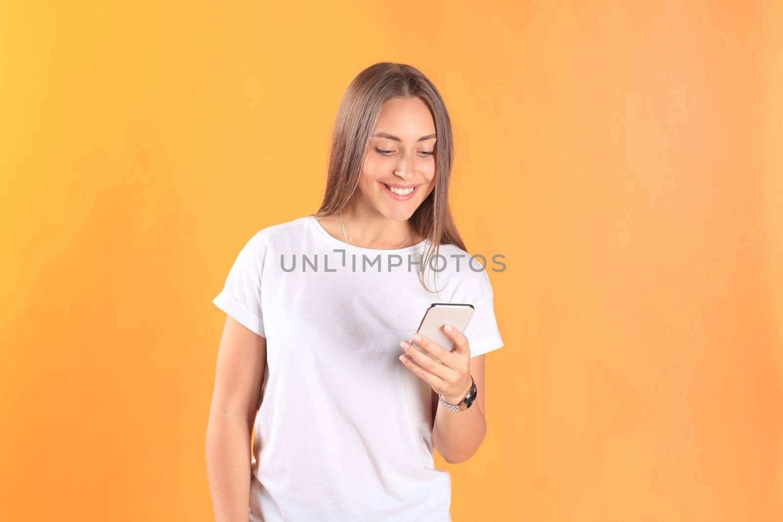 Young woman dressed in basic clothing isolated on yellow background, using mobile phone.