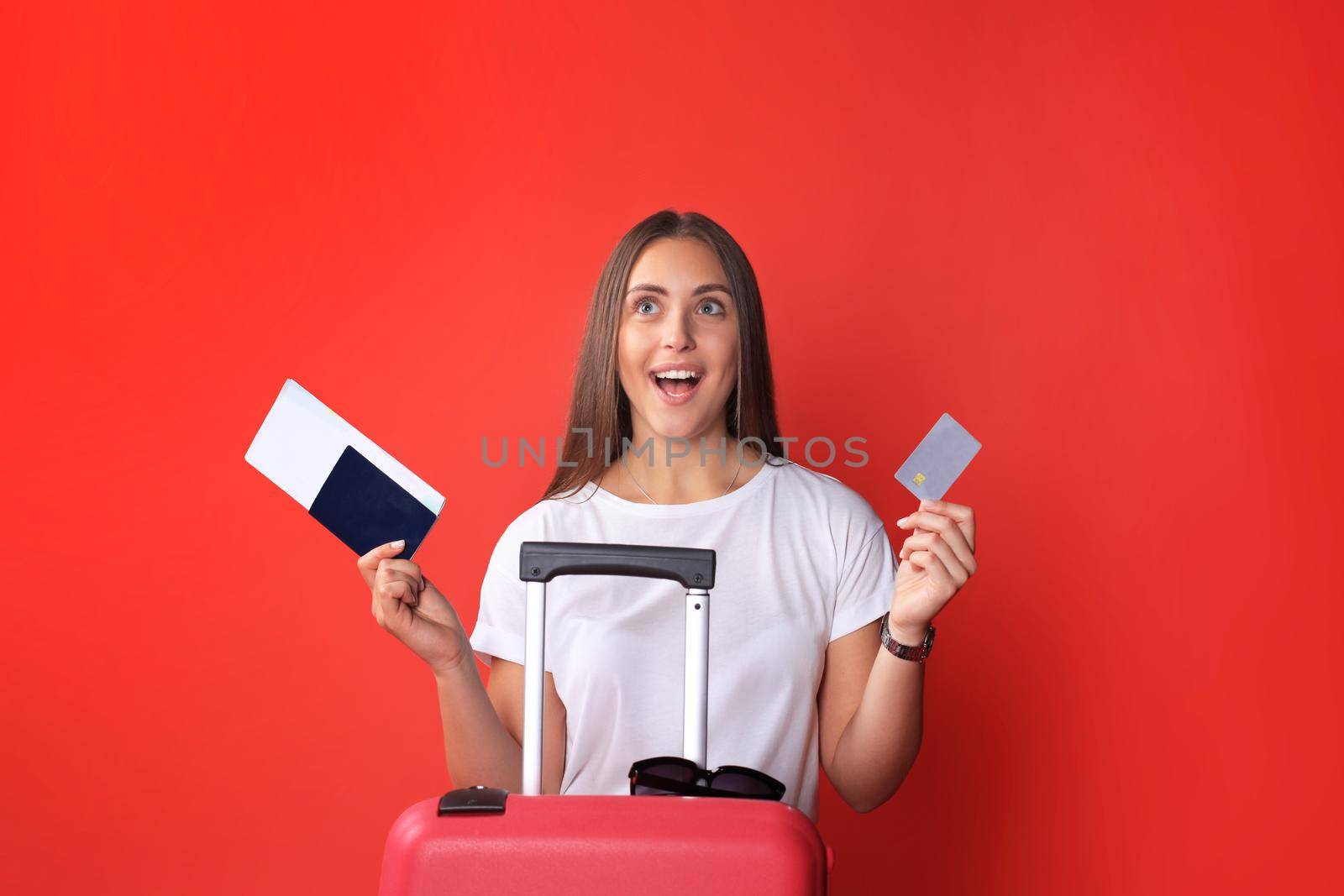 Young tourist girl in summer casual clothes, with sunglasses, red suitcase, passport isolated on red background. by tsyhun