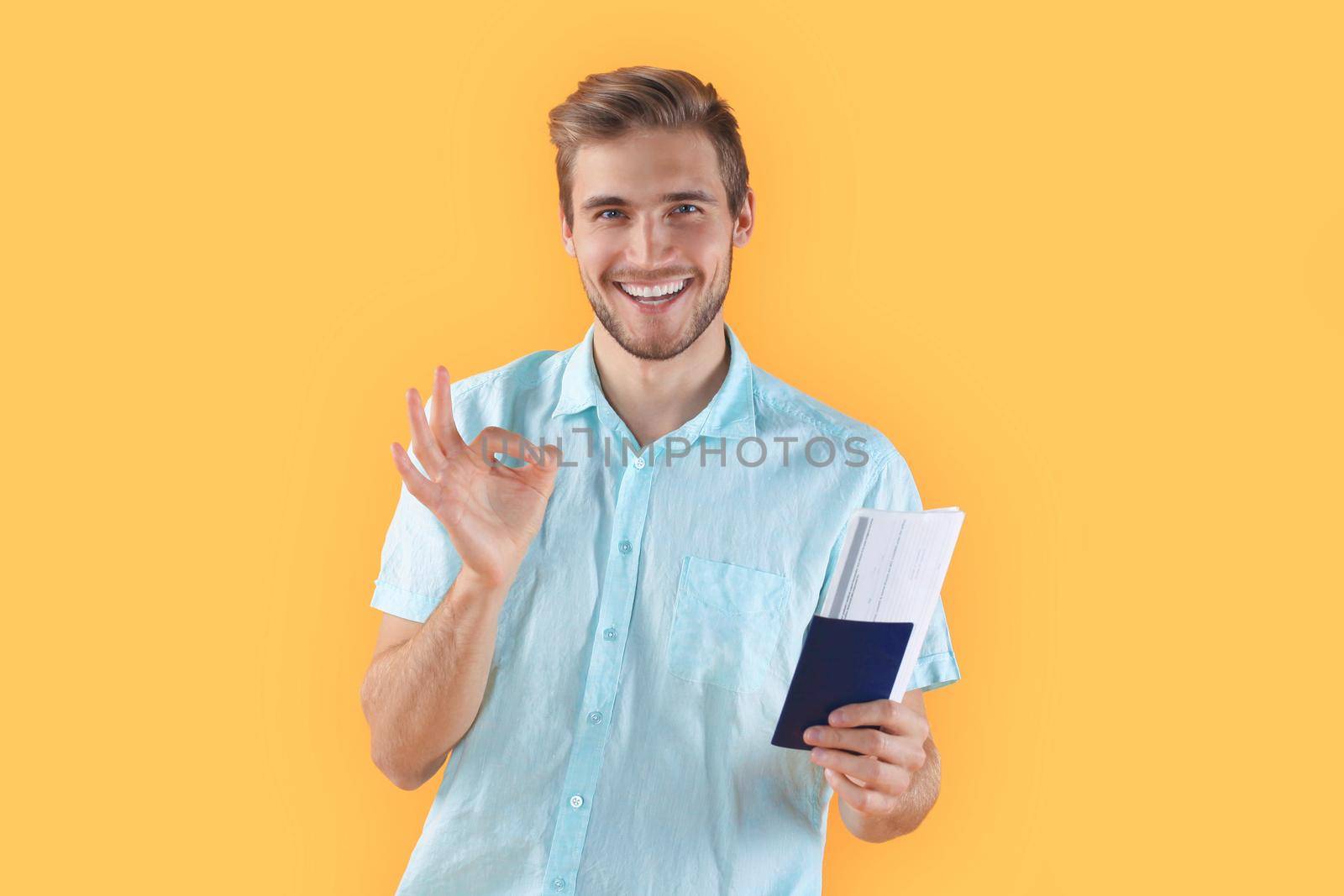 Young man isolated over yellow background holding passport pointing