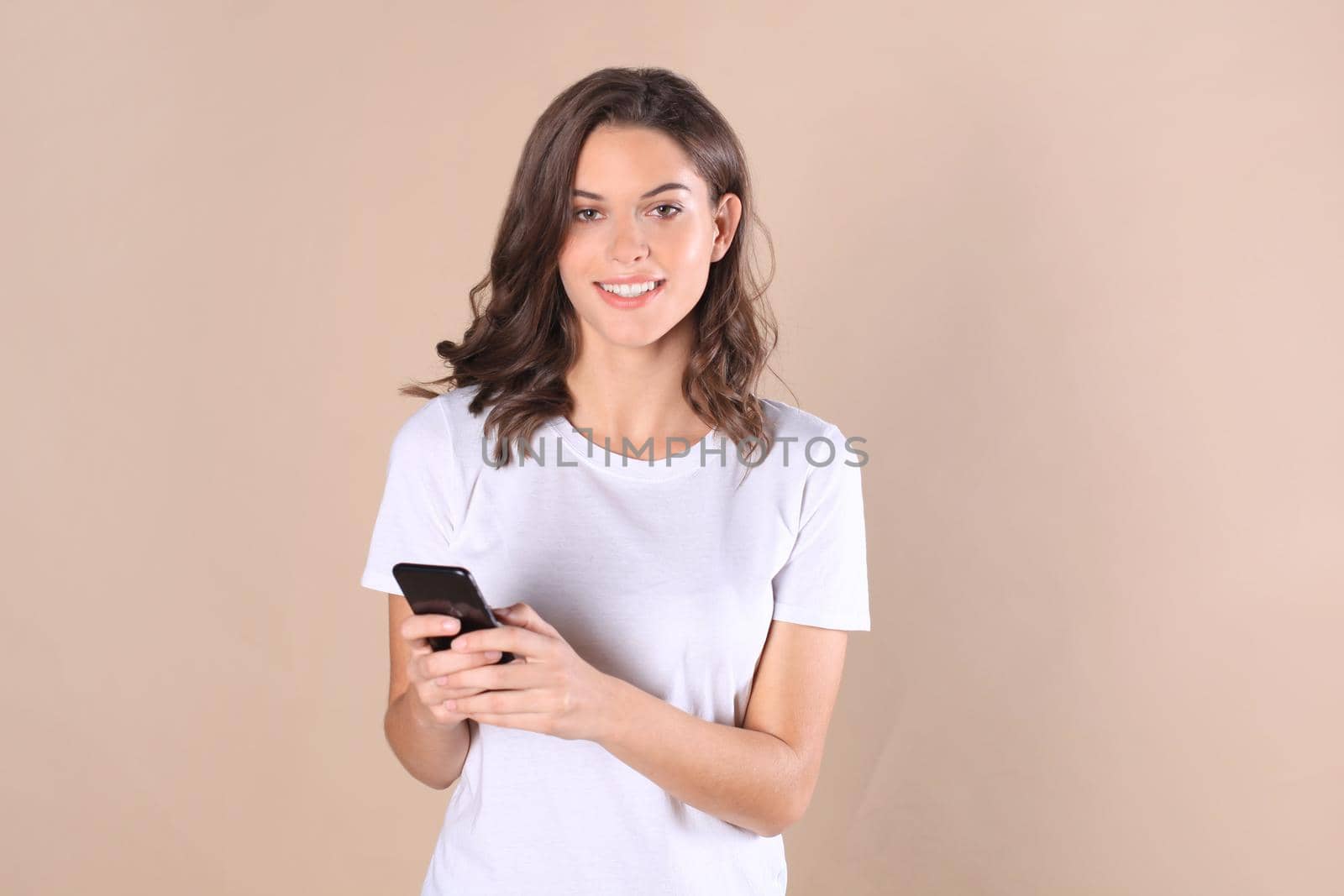 Young woman dressed in basic clothing isolated on beige background, using mobile phone by tsyhun
