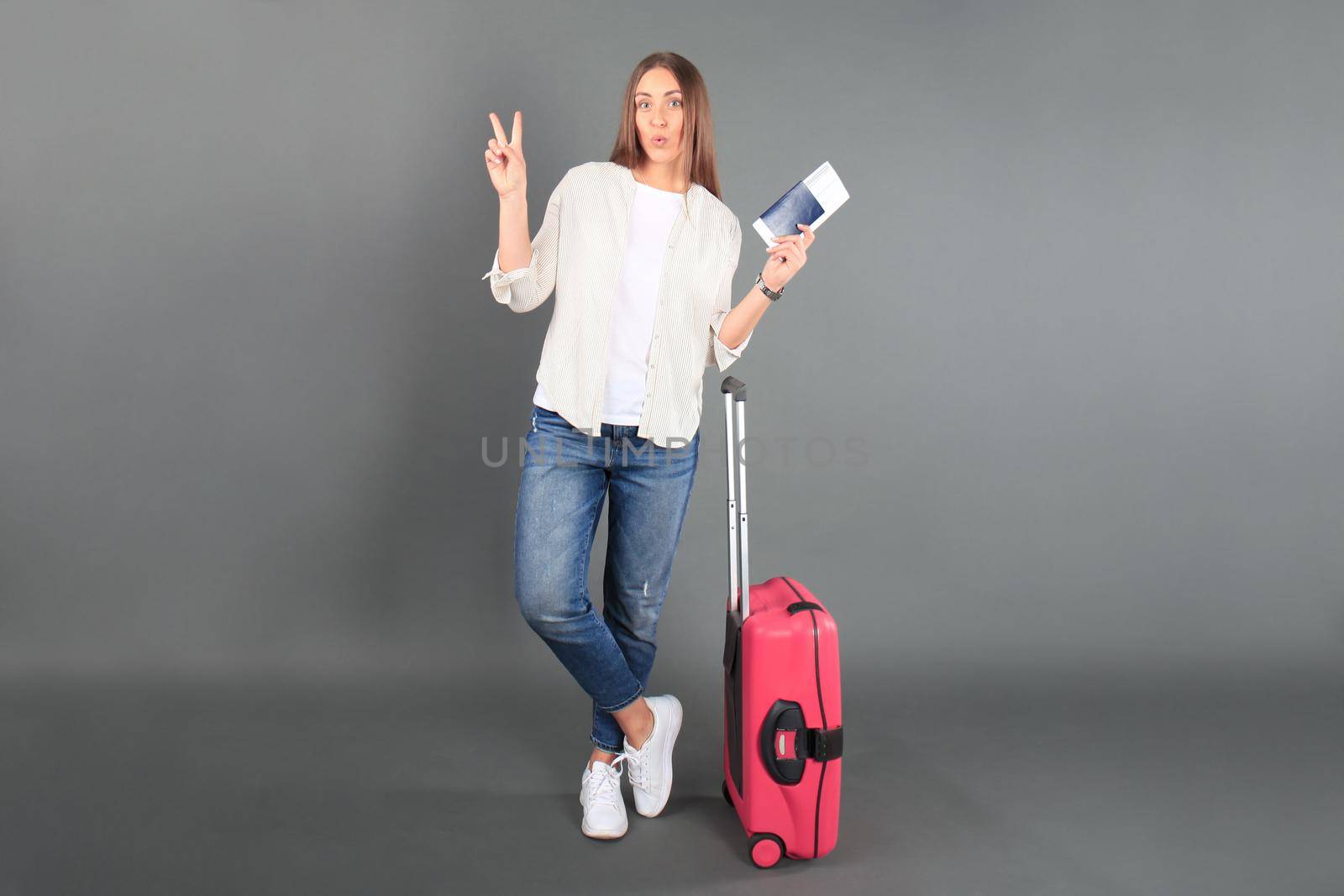 Young tourist girl in summer casual clothes, with sunglasses, red suitcase, passport, tickets isolated grey background.