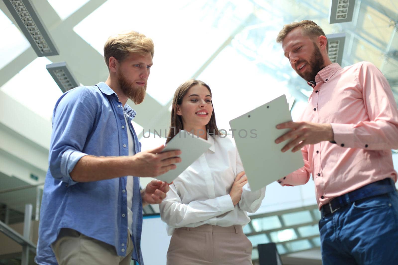Young modern people in smart casual wear discussing business while standing in creative office.