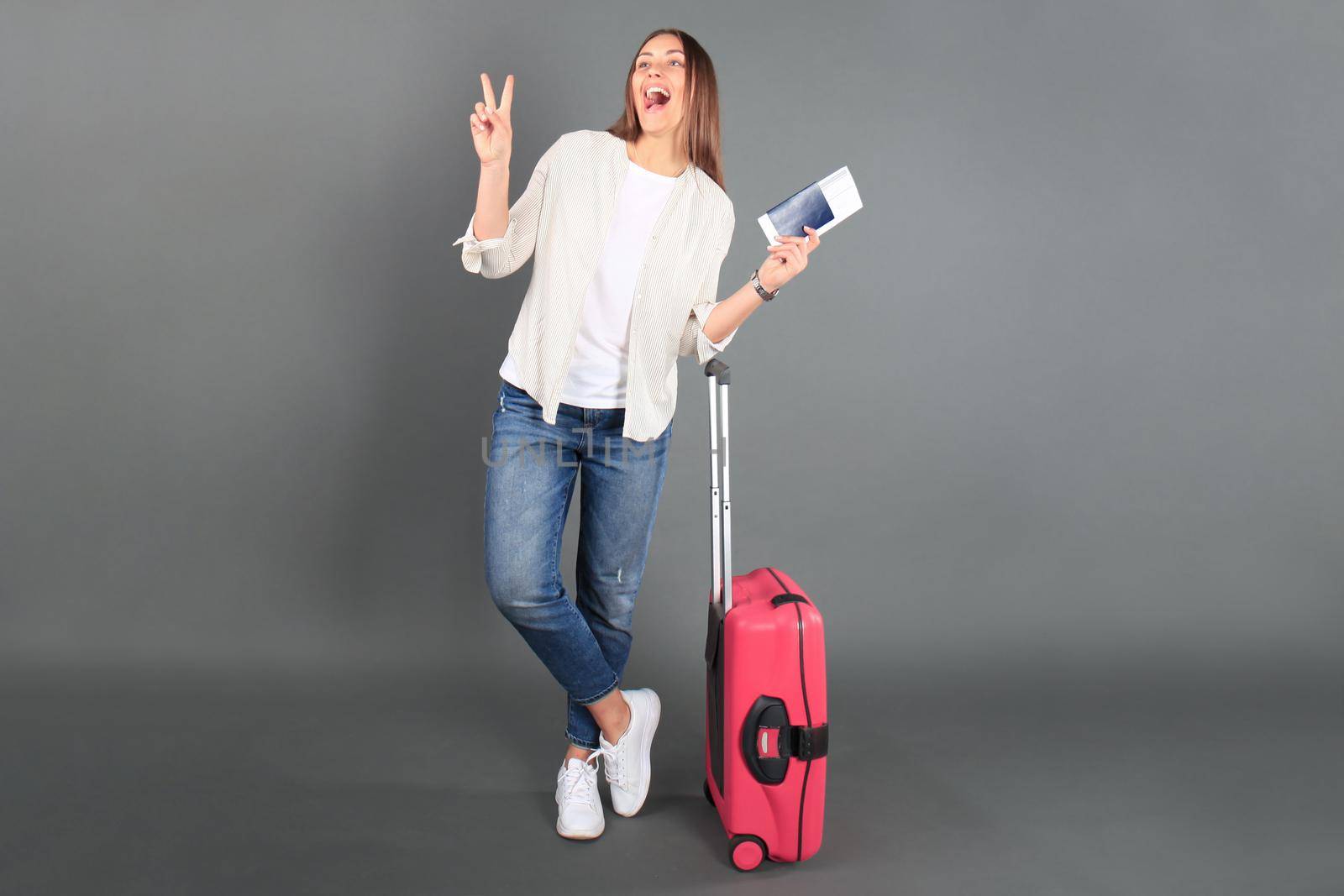 Young tourist girl in summer casual clothes, with sunglasses, red suitcase, passport, tickets isolated grey background.