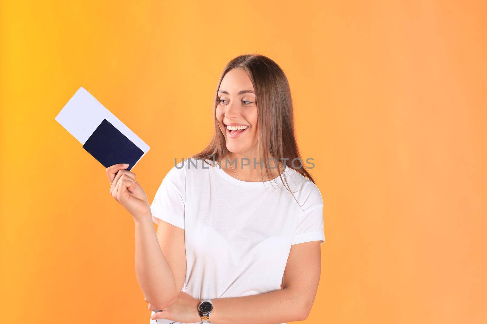 Excited young woman tourist standing isolated on yellow background holding passport with tickets.