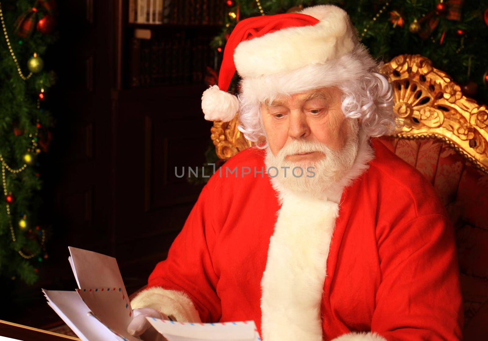 Santa sitting at the Christmas tree, holding Christmas letters and having a rest by the fireplace.